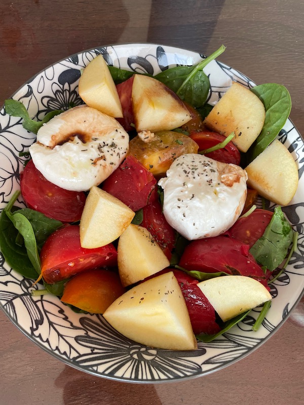 Bowl of spinach, burrata cheese, tomatoes, and apples