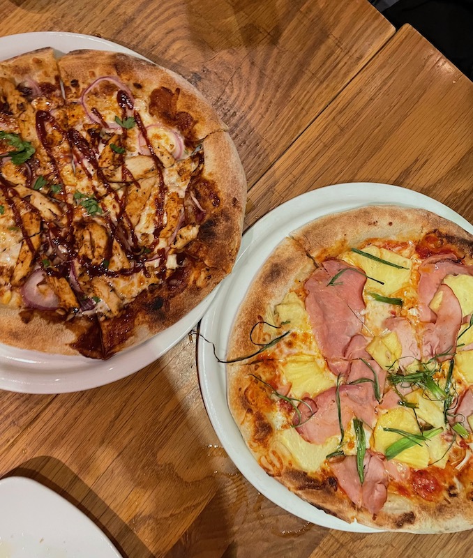 Two pizzas, one with barbecue and one with ham and pineapple